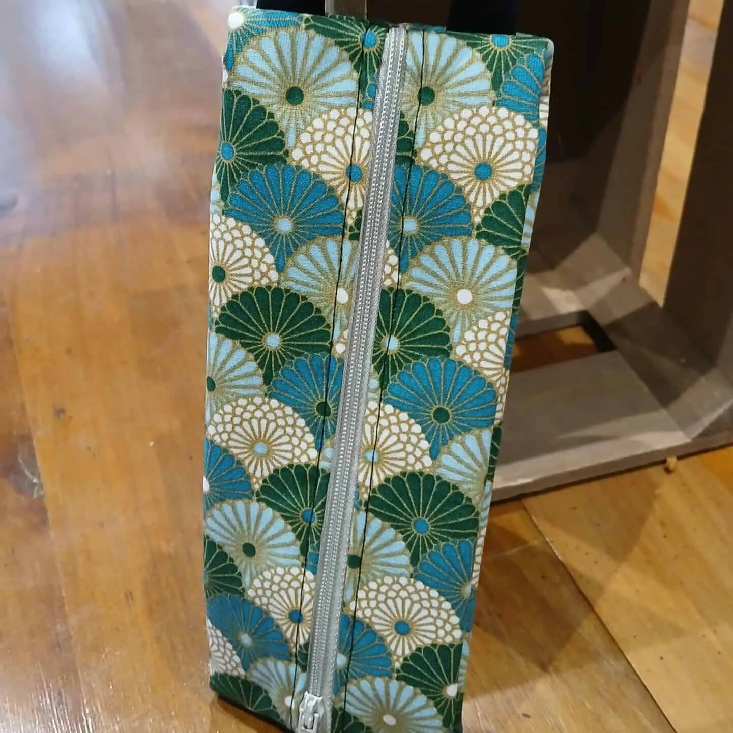 Trousse en tissu avec motifs de fleurs dorées et bleues, fermeture éclair grise et anse pratique